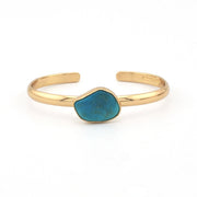Gold bracelet with a blue stone on a white background