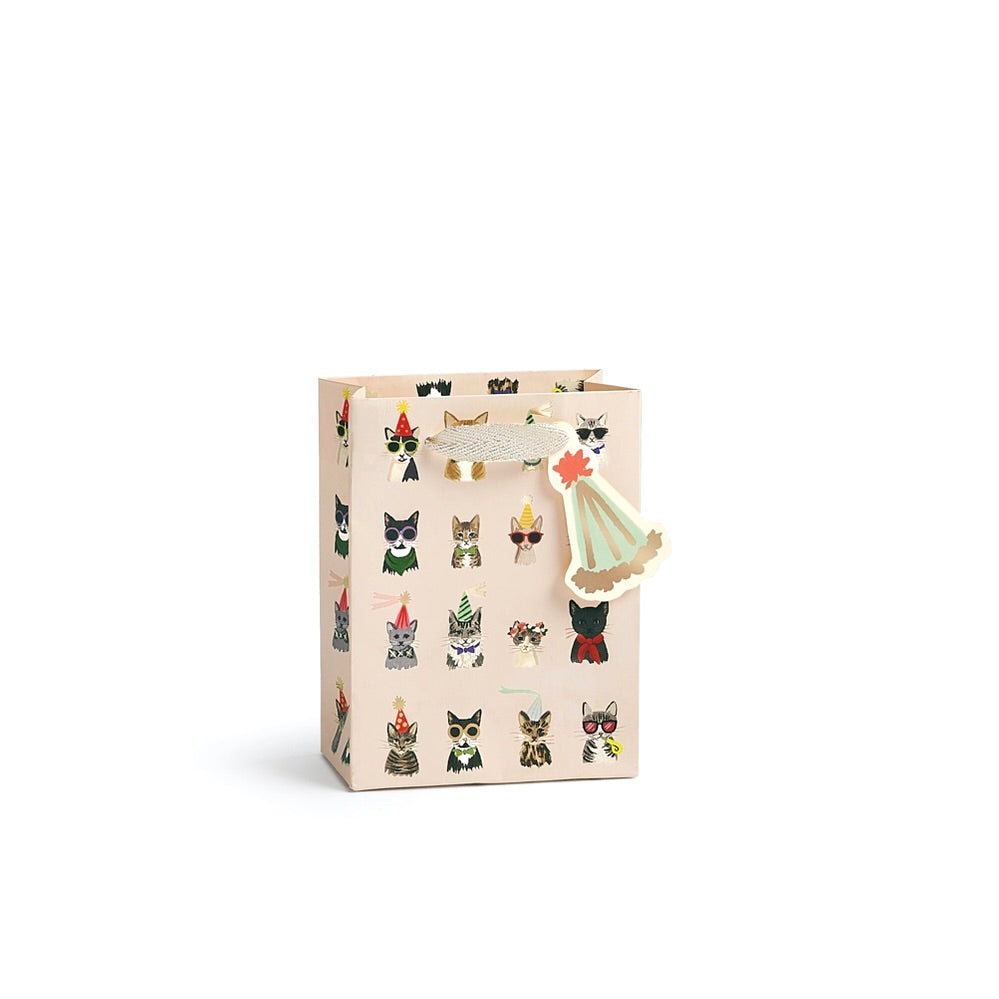 A beige gift bag decorated with a pattern of small illustrated cats in various outfits, featuring a decorative paper cat topper on the handle, set against a plain white background.