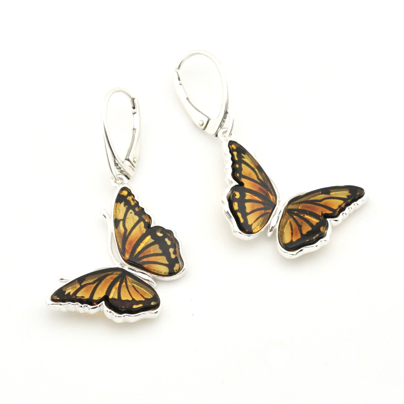 A pair of butterfly drop earrings with orange and black patterned wings set in silver, suspended from silver leverback hooks on a white background.