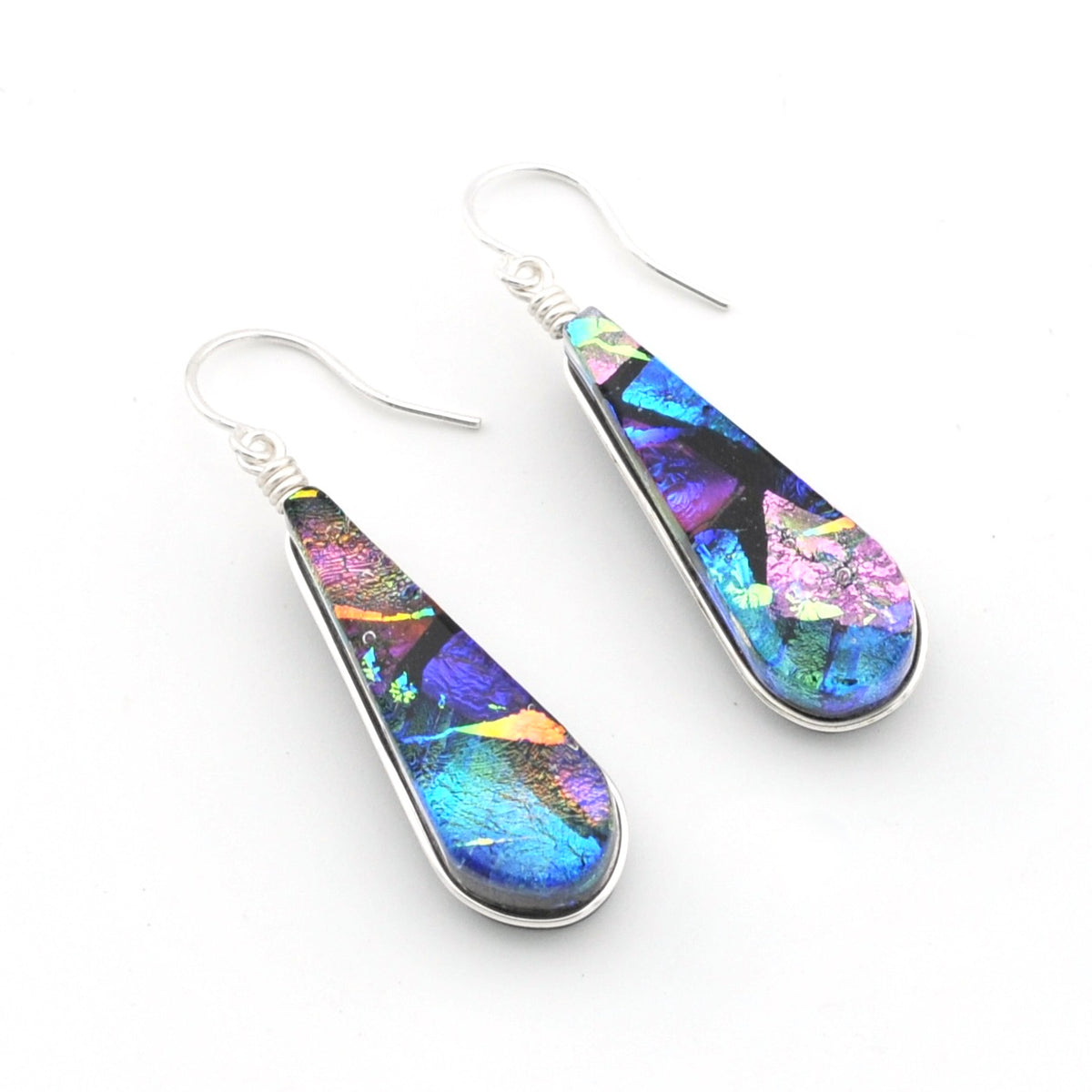 A pair of teardrop-shaped dangle earrings featuring dichroic glass with vibrant blue, purple, pink, and gold hues, set in silver-tone metal with fishhook wires on a white background.