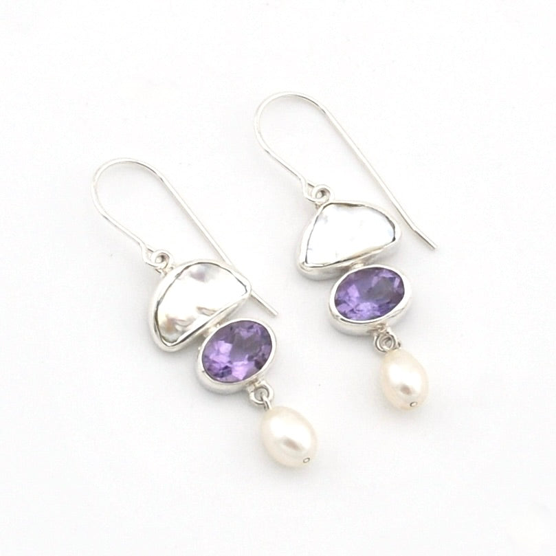 A pair of silver drop earrings featuring oval purple amethyst gemstones and dangling white freshwater pearls, set against a plain white background.