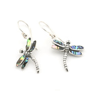 A pair of silver dragonfly drop earrings featuring iridescent abalone shell wings that shimmer with blue, green, and pink hues, set against a plain white background.