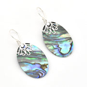 A pair of silver dangle earrings featuring oval abalone shell with iridescent blue, green, and gray patterns, set against a plain white background.