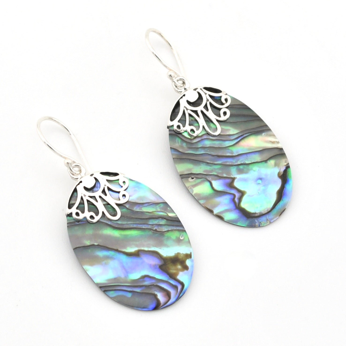 A pair of silver dangle earrings featuring oval abalone shell with iridescent blue, green, and gray patterns, set against a plain white background.