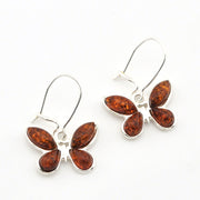 A pair of butterfly-shaped drop earrings featuring polished amber-brown stones in silver settings, suspended from silver fishhook wires on a plain white background.