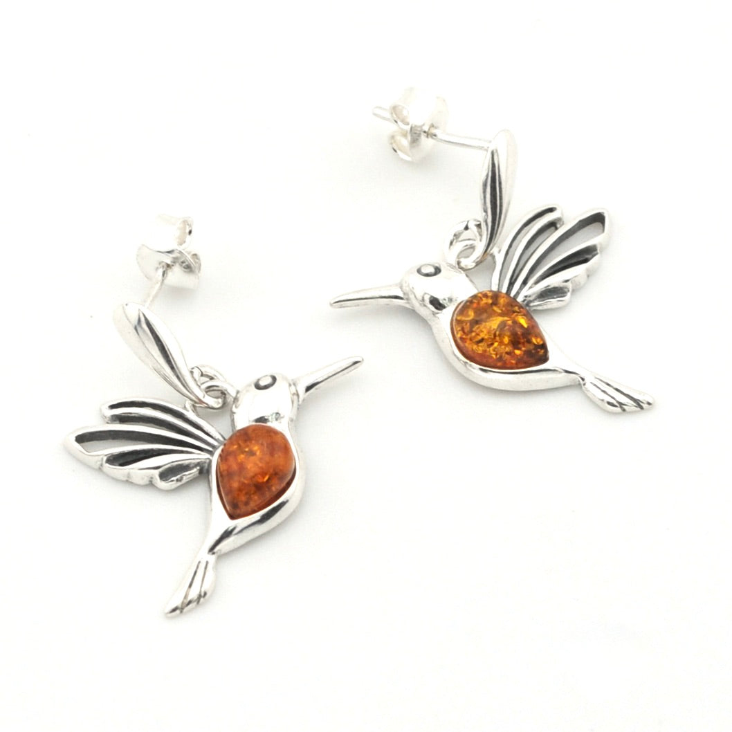 A pair of sterling silver hummingbird post dangle earrings with polished amber-colored gemstones in their bellies, shown on a clean white background.