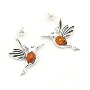 A pair of sterling silver hummingbird post dangle earrings with polished amber-colored gemstones in their bellies, shown on a clean white background.