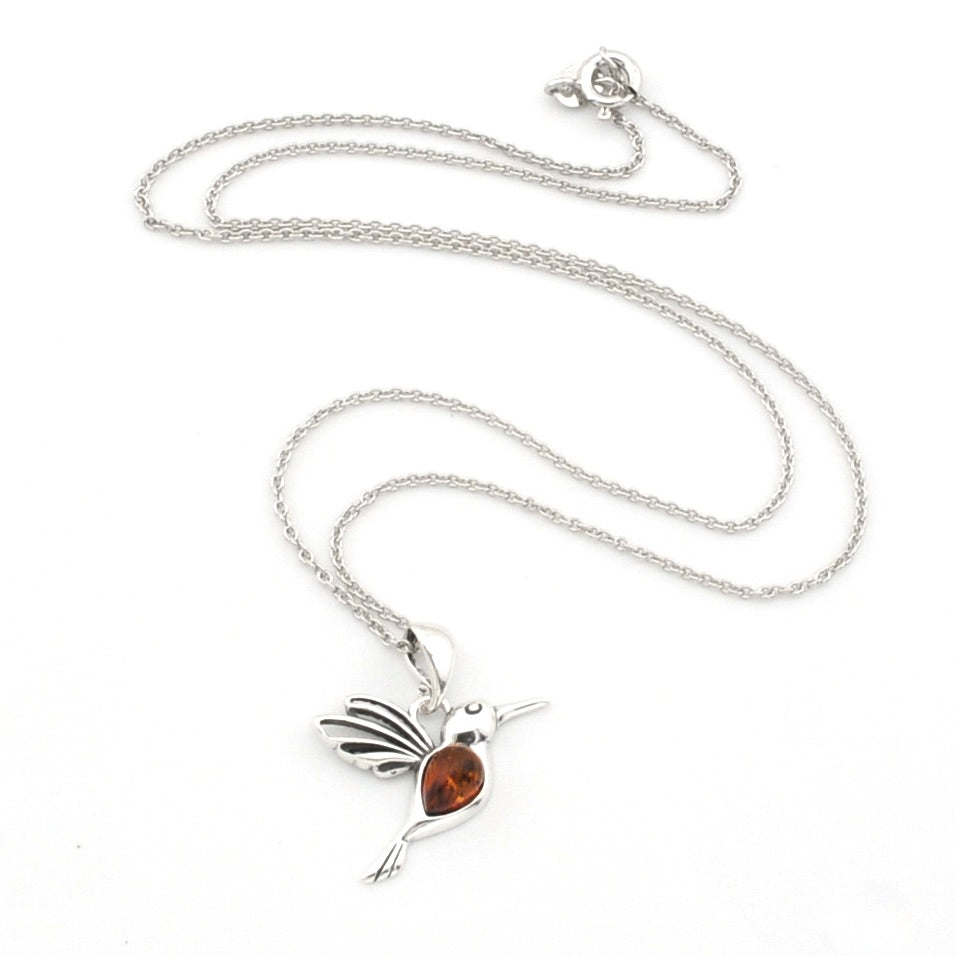 A silver-toned hummingbird pendant necklace with a small amber-orange heart-shaped gemstone in the center, displayed on a clean white background.