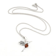 A silver-toned hummingbird pendant necklace with a small amber-orange heart-shaped gemstone in the center, displayed on a clean white background.