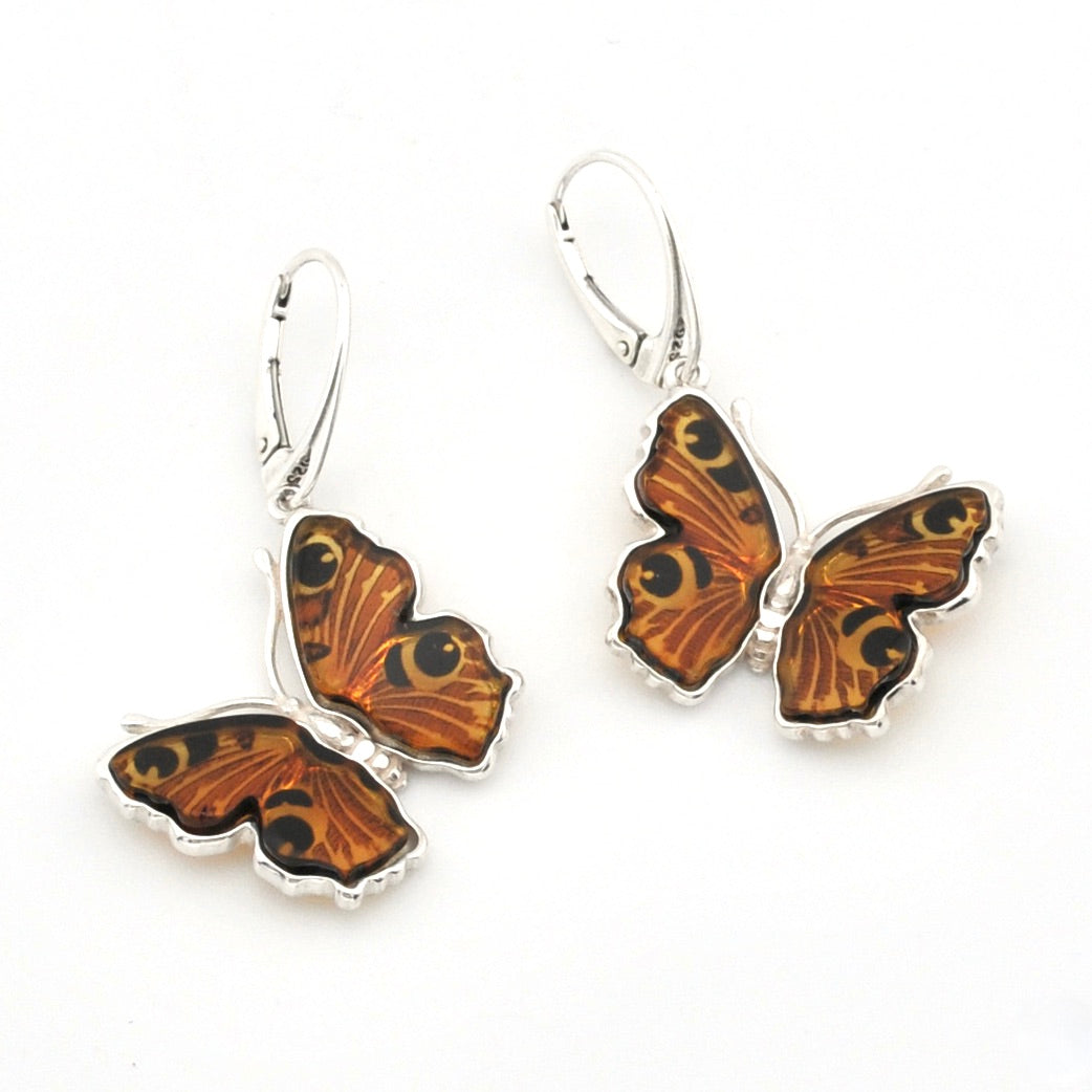 A pair of silver leverback earrings featuring butterfly wings with orange, brown, and black patterned inlay, displayed on a clean white background.