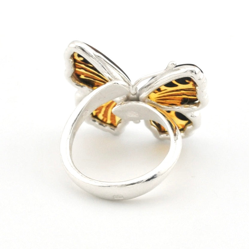 A silver ring designed as a butterfly, featuring one wing half in polished silver and the other half in gold and black enamel, set against a plain white background.