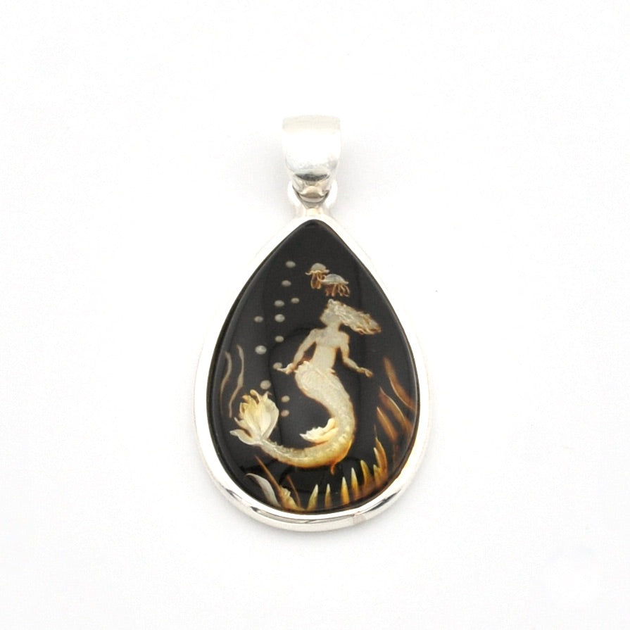 A teardrop-shaped pendant featuring a detailed mermaid illustration in cream and gold on a dark black background, set in a polished silver-tone metal bezel with a silver bail, photographed against a plain white background.