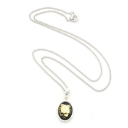 A silver chain necklace with an oval pendant featuring a black background and a vintage-style illustration of a yellow flower in a silver frame, displayed on a clean white background.