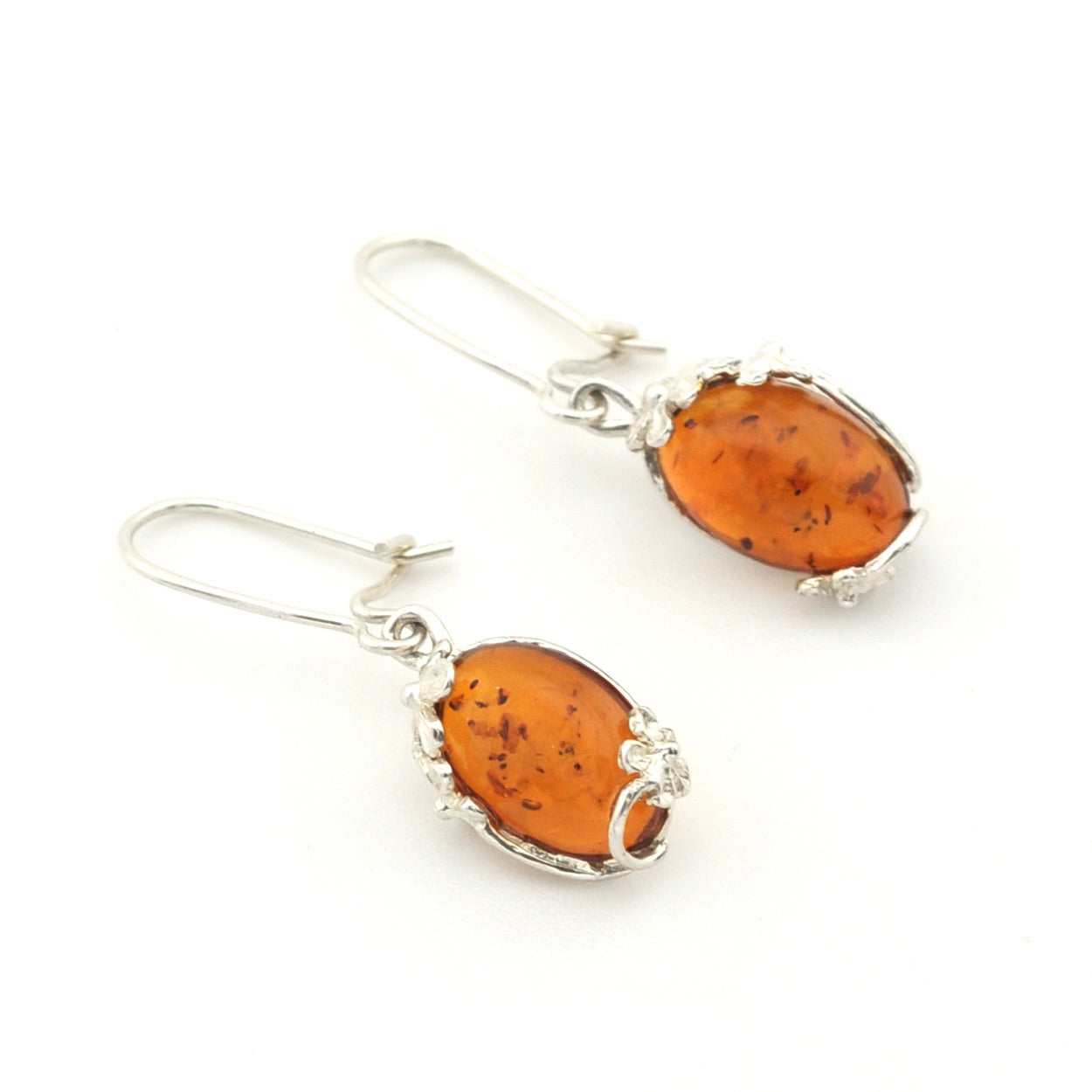 A pair of silver drop earrings featuring oval amber-colored stones with dark inclusions, set in silver bezel settings with small clear stones, on a white background.