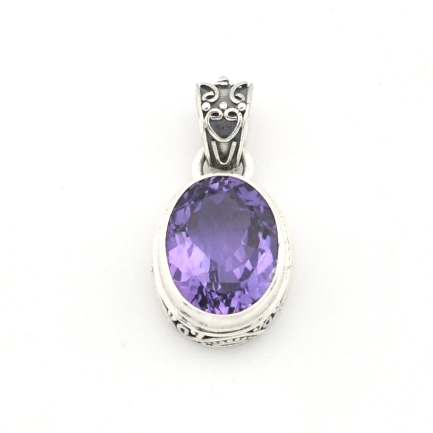 An oval-cut purple amethyst pendant in a silver-toned bezel setting with an ornate decorative bail, shown against a plain white background.