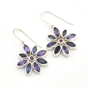 A pair of silver dangle earrings featuring a flower design with marquise-cut purple gemstones and a small round pink center stone, shown on a plain white background.