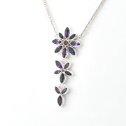 A silver pendant necklace featuring three vertically stacked flower clusters with marquise-cut purple gemstones, shown against a plain white background.