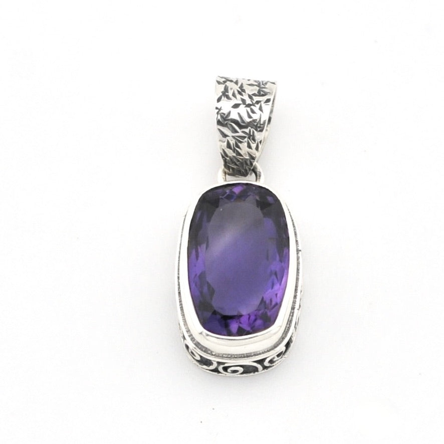 A sterling silver pendant featuring a large, bezel-set oval purple amethyst gemstone, with an engraved textured bail at the top, shown on a plain white background.