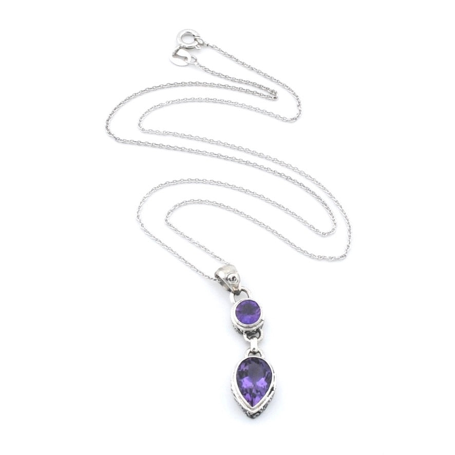 A silver-toned necklace featuring a dual gemstone pendant with a small oval purple stone and a larger teardrop-shaped purple stone, displayed on a clean white background.