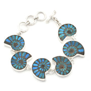 A silver-toned bracelet featuring six round ammolite shell inlays with vibrant blue and green iridescent patterns, set in polished silver on a white background.