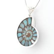 A silver pendant necklace featuring a polished ammolite shell-shaped stone with a spiral pattern of light blue, turquoise, and brown, suspended from a silver chain on a white background.