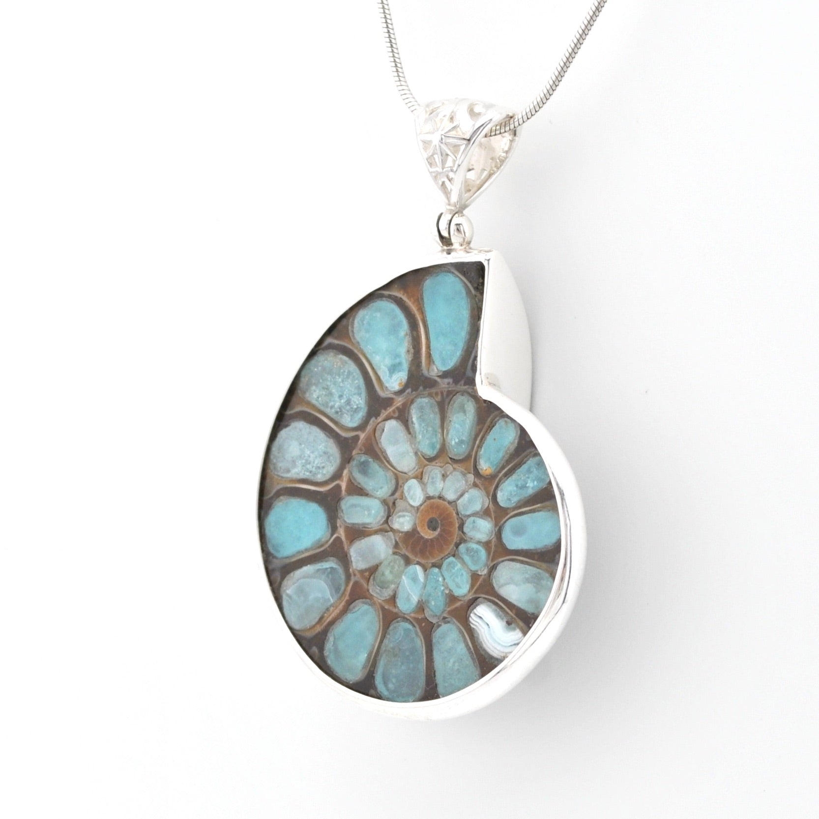 A silver pendant necklace featuring a polished ammolite shell-shaped stone with a spiral pattern of light blue, turquoise, and brown, suspended from a silver chain on a white background.
