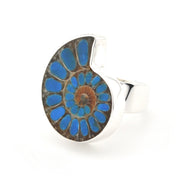 A silver ring featuring a large, circular inlay of an ammonite fossil showing vibrant blue, brown, and tan layers, set against a plain white background.