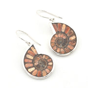 A pair of silver drop earrings featuring circular spiral inlays of metallic bronze, copper, and brown segments, suspended from silver French hooks on a white background.