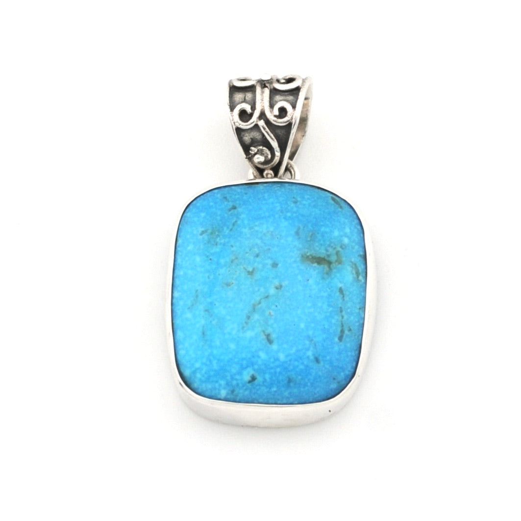 A silver pendant featuring a rectangular turquoise-blue stone with natural darker inclusions, set in a polished silver bezel with an ornate scrollwork bail.