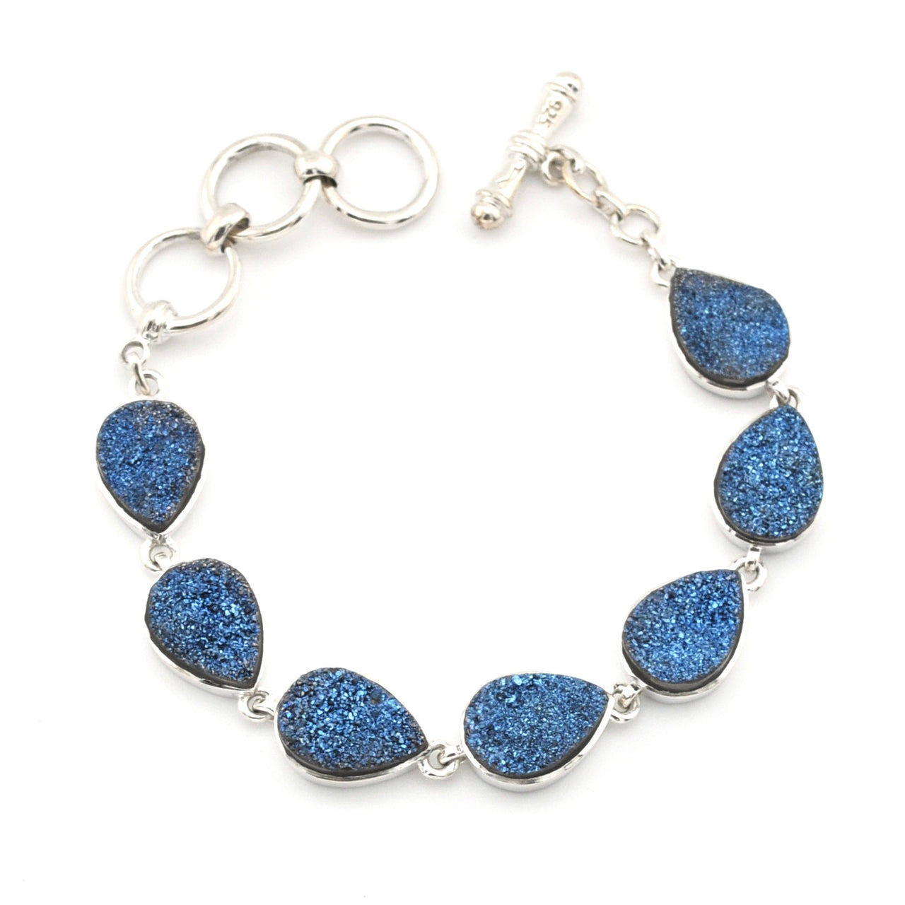 A silver-tone bracelet featuring seven teardrop-shaped blue glitter druse stones set in silver bezels, connected by silver rings and a toggle clasp, shown on a plain white background.