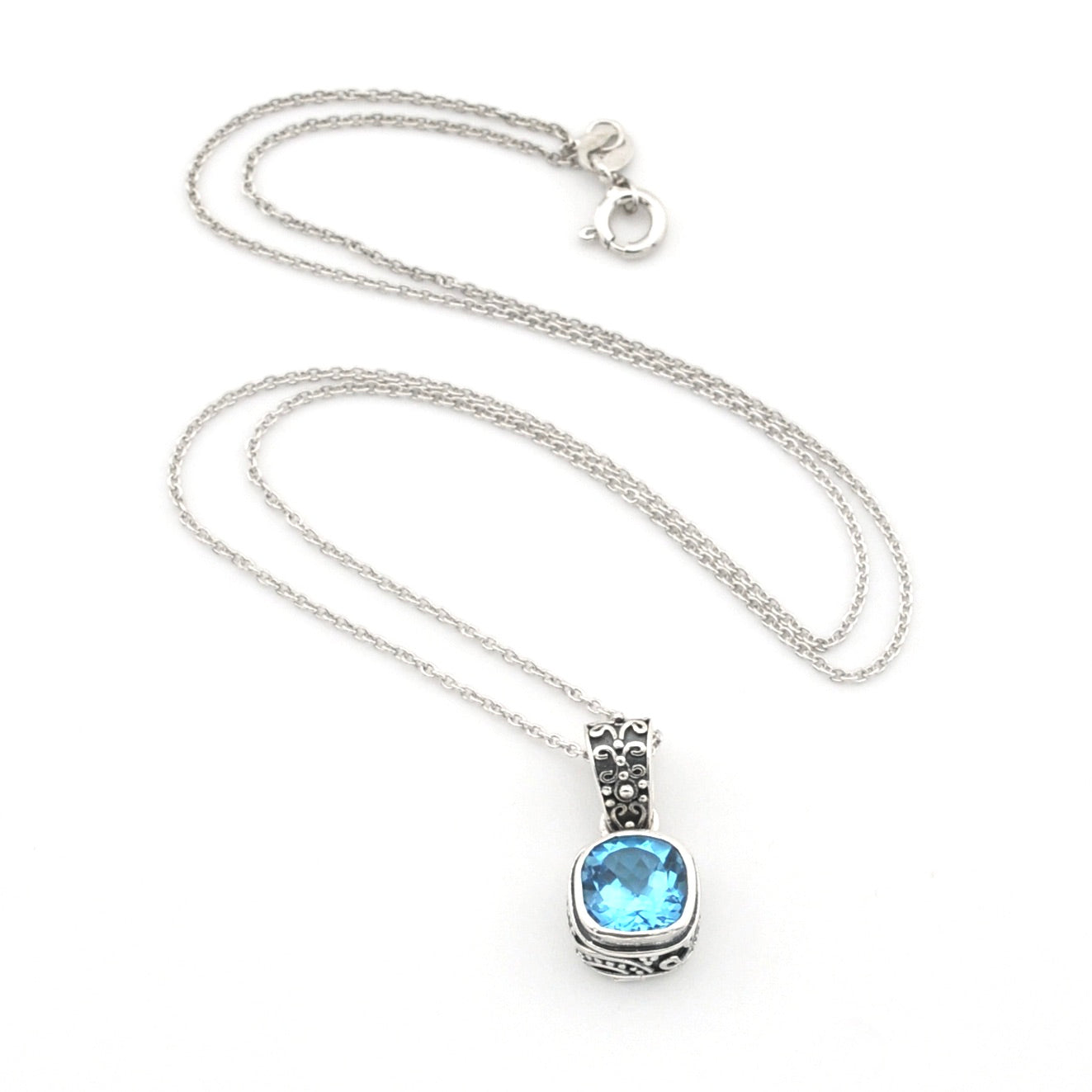 A silver chain necklace with a square pendant featuring a light blue gemstone and silver filigree detailing, displayed on a clean white background.