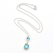 A silver necklace featuring a teardrop-shaped abalone shell pendant and a small round blue gemstone, displayed on a clean white background.