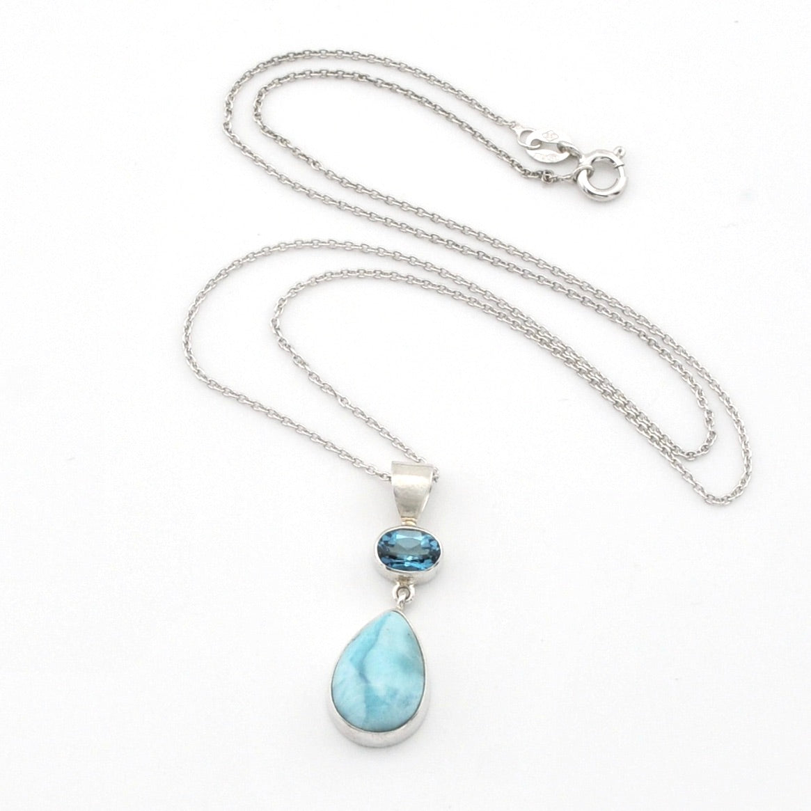 Silver necklace with a teardrop-shaped light blue larimar stone pendant and a small oval dark blue gemstone accent, displayed on a white background.