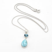 Silver necklace with a teardrop-shaped light blue larimar stone pendant and a small oval dark blue gemstone accent, displayed on a white background.