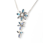 A silver-toned dangle necklace featuring three vertical rows of flower-shaped settings with marquise-cut blue iridescent stones and a small round pearl in the center of the top flower, shown on a white background.