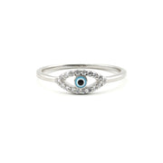 A silver-toned evil eye ring featuring a central blue and black eye motif surrounded by small clear stones, set against a plain white background.