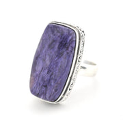 A silver ring featuring a large, rectangular purple stone with natural marbled patterns, set in an ornate silver bezel on a white background.