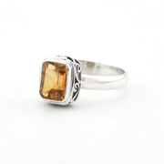 A silver ring featuring a rectangular amber-yellow gemstone with decorative black oxidized scrollwork on the band, set against a plain white background.
