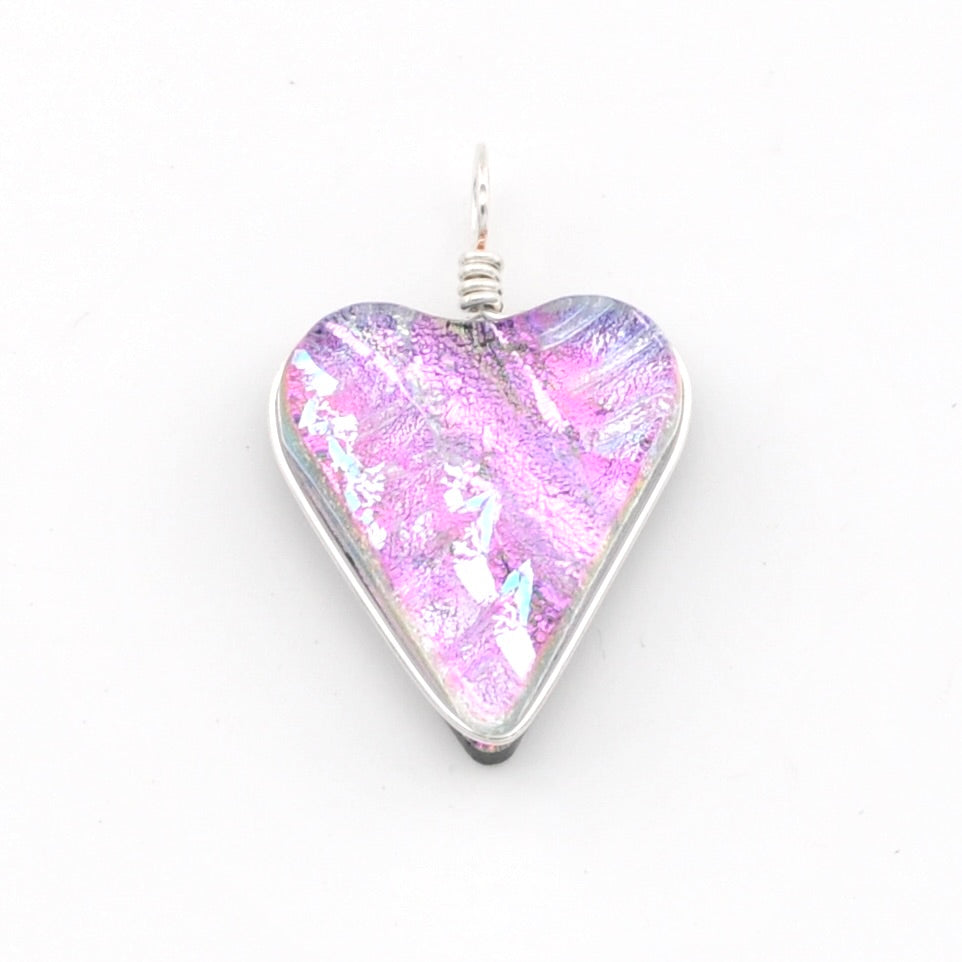 A heart-shaped glass pendant with a vibrant pink, purple, and blue iridescent pattern, set in a silver-toned metal bezel with a silver wire-wrapped loop at the top, shown on a plain white background.