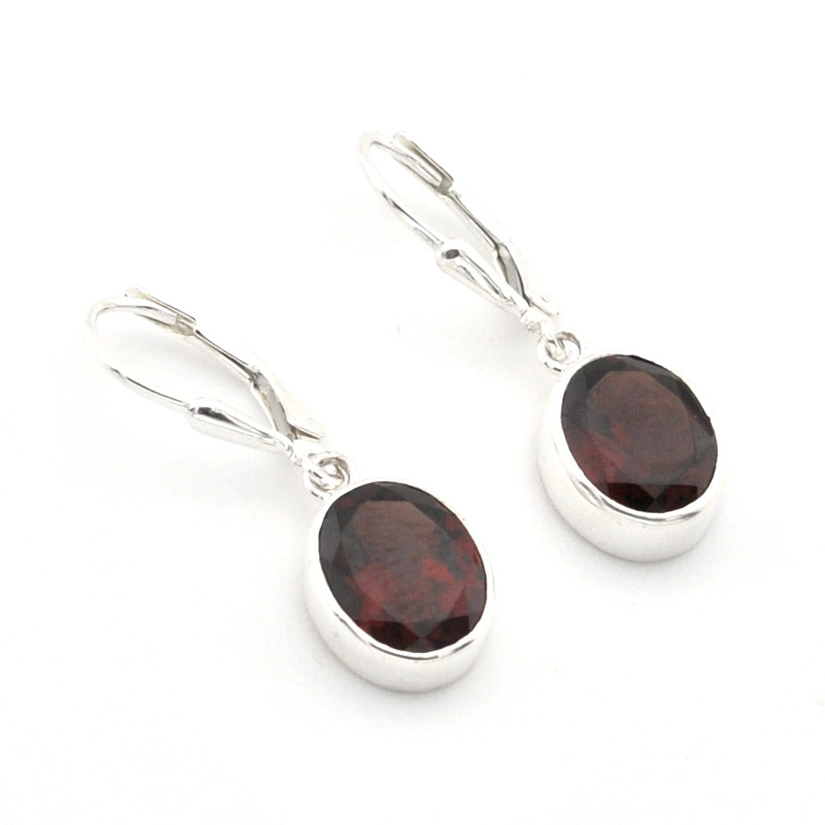 A pair of silver leverback drop earrings with oval dark red garnet gemstones, shown on a clean white background.