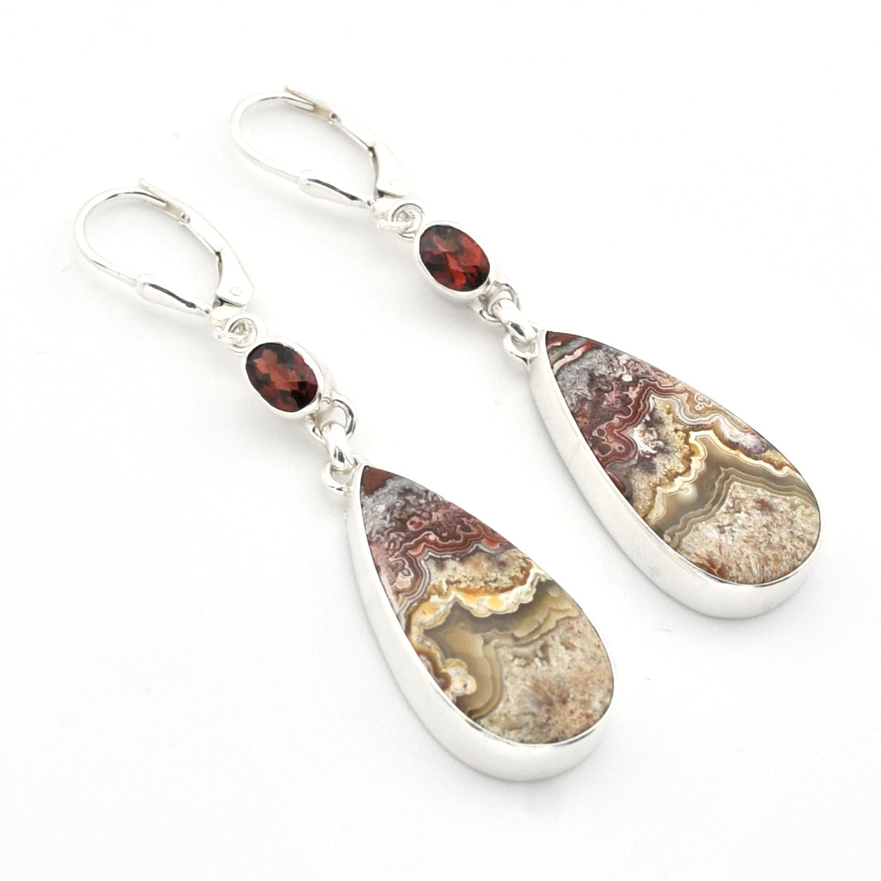 A pair of silver leverback earrings featuring teardrop-shaped agate stone pendants with natural banded patterns in brown, beige, and gray, accented by small round dark red garnet beads.