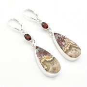 A pair of silver leverback earrings featuring teardrop-shaped agate stone pendants with natural banded patterns in brown, beige, and gray, accented by small round dark red garnet beads.
