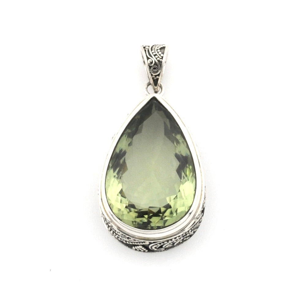 A teardrop-shaped pendant featuring a faceted olive-green gemstone in a silver-toned metal bezel with ornate engraved details on the sides and bail, set against a plain white background.
