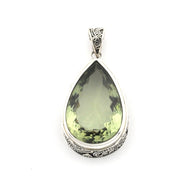 A teardrop-shaped pendant featuring a faceted olive-green gemstone in a silver-toned metal bezel with ornate engraved details on the sides and bail, set against a plain white background.