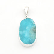 A silver pendant featuring a large, irregularly shaped turquoise-blue stone with natural white and gray marbling, set against a plain white background.