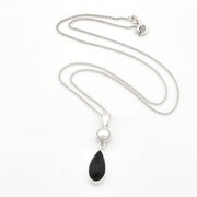 A silver necklace featuring a teardrop-shaped black onyx pendant and a small round white pearl, displayed on a clean white background.