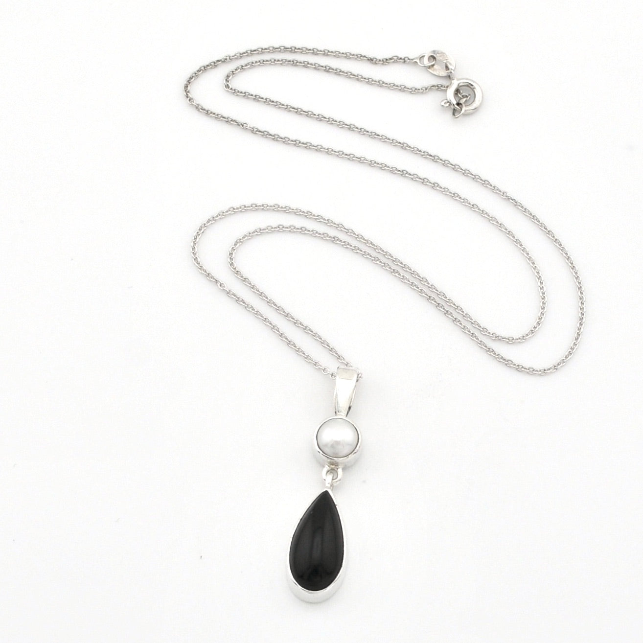 A silver necklace featuring a teardrop-shaped black onyx pendant and a small round white pearl, displayed on a clean white background.