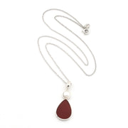 A silver chain necklace featuring a teardrop-shaped dark red pendant with a silver border and a small white pearl accent above it, displayed on a clean white background.