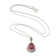 A silver necklace featuring a teardrop-shaped pink gemstone pendant in a textured bezel setting, displayed on a clean white background.