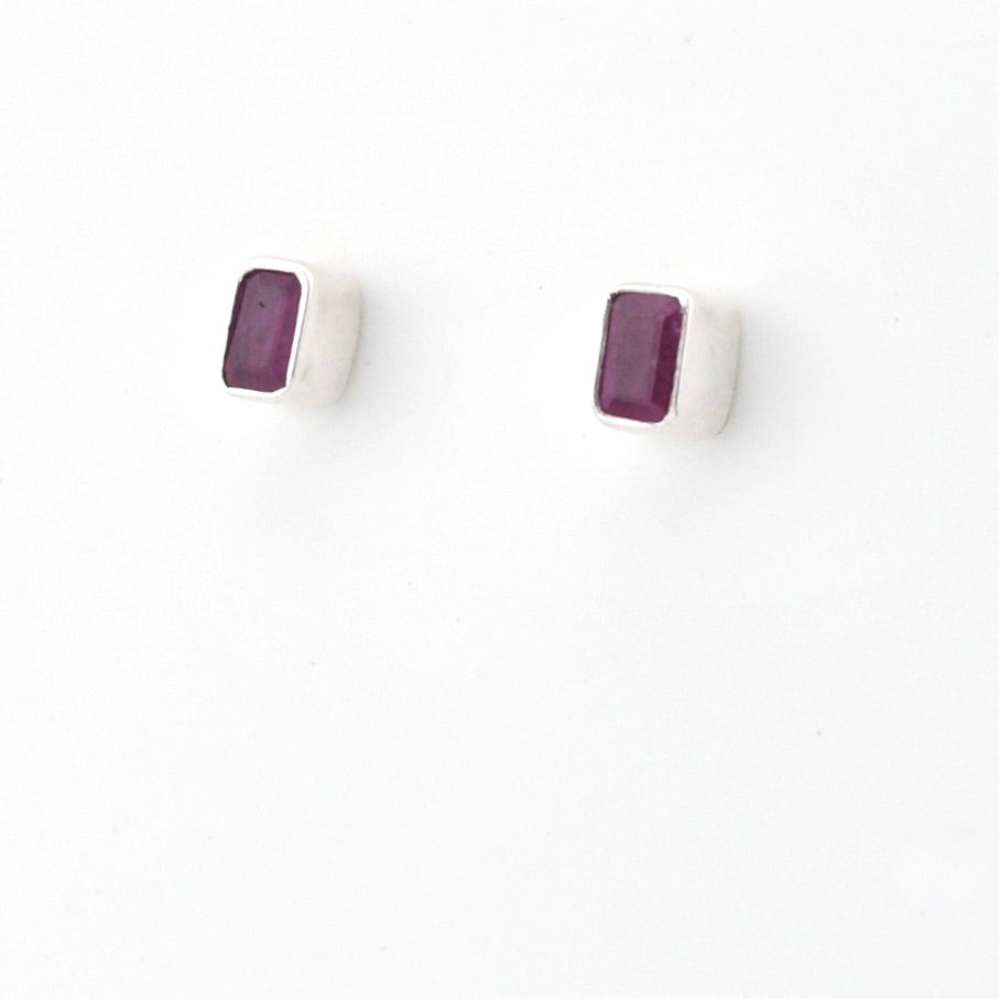 A pair of silver stud earrings with small rectangular purple gemstones, shown on a plain white background.